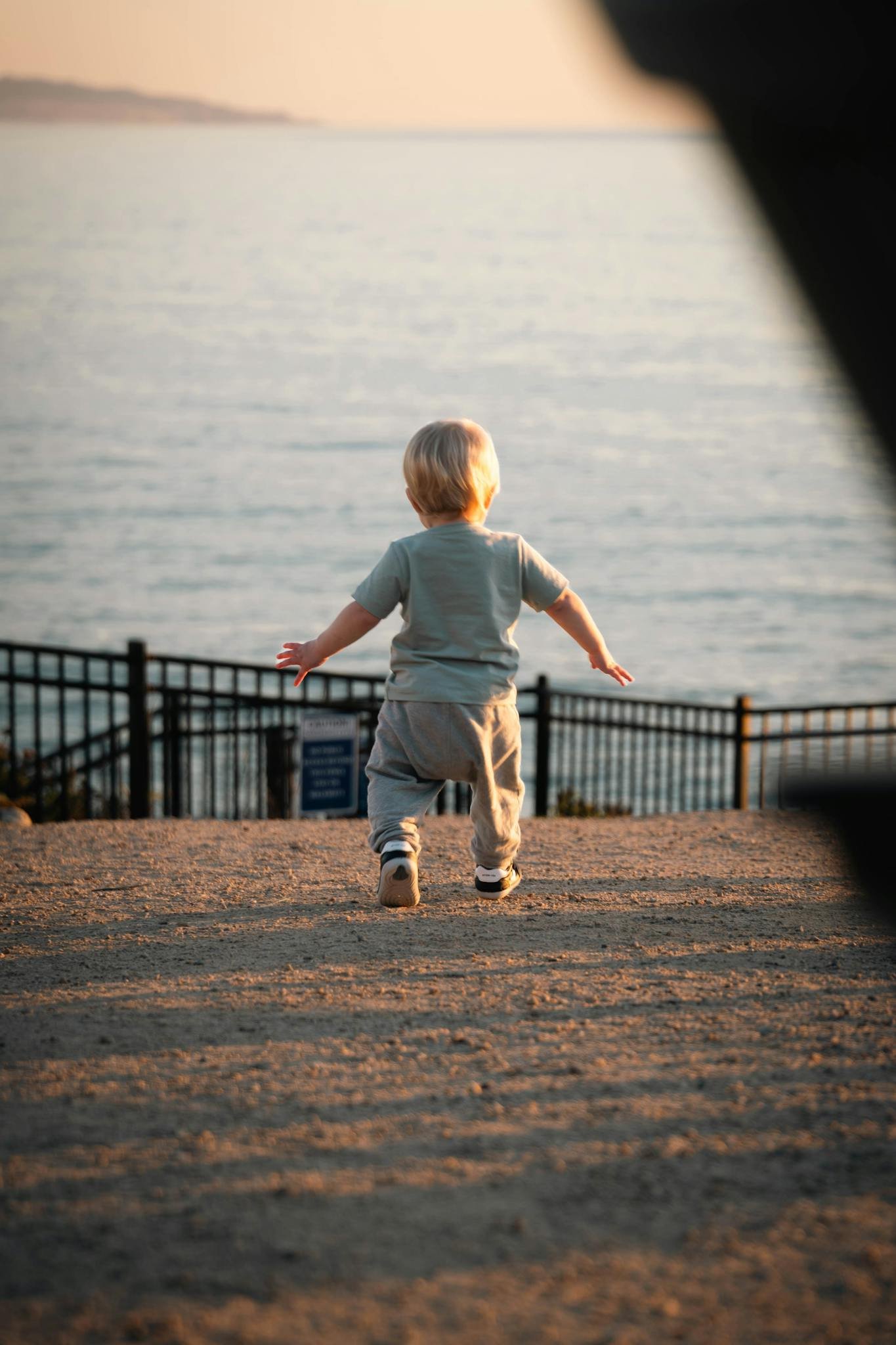 A toddler walks towards the ocean at Pismo Beach during sunset, capturing a serene and adventurous moment.