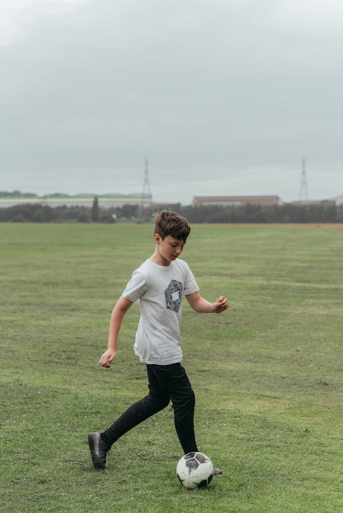 A young boy enjoying a game of soccer on a wide green field during the day.