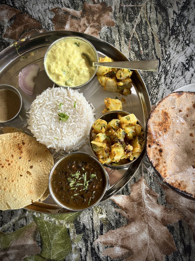 Authentic Indian thali with rice, curries, flatbread, and papad on a colorful background.